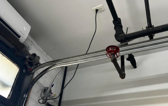 Pipes, wiring, and a mini-split unit are visible on a ceiling in an interior space.