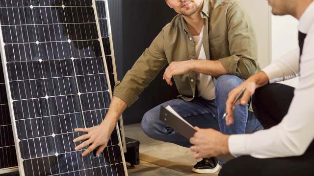 Two men discussing solar panels, one pointing to a solar panel while the other holds a notepad.