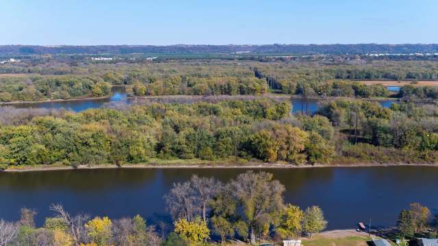 A river meanders through a landscape of trees and greenery under a clear blue sky.