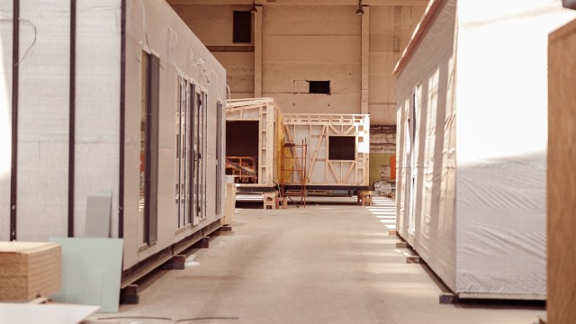 An interior view of a warehouse with modular buildings and construction materials arranged along the pathway.