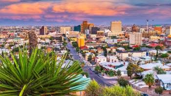 A view of the El Paso, Texas, city skyline with buildings and houses under a colorful sky.
