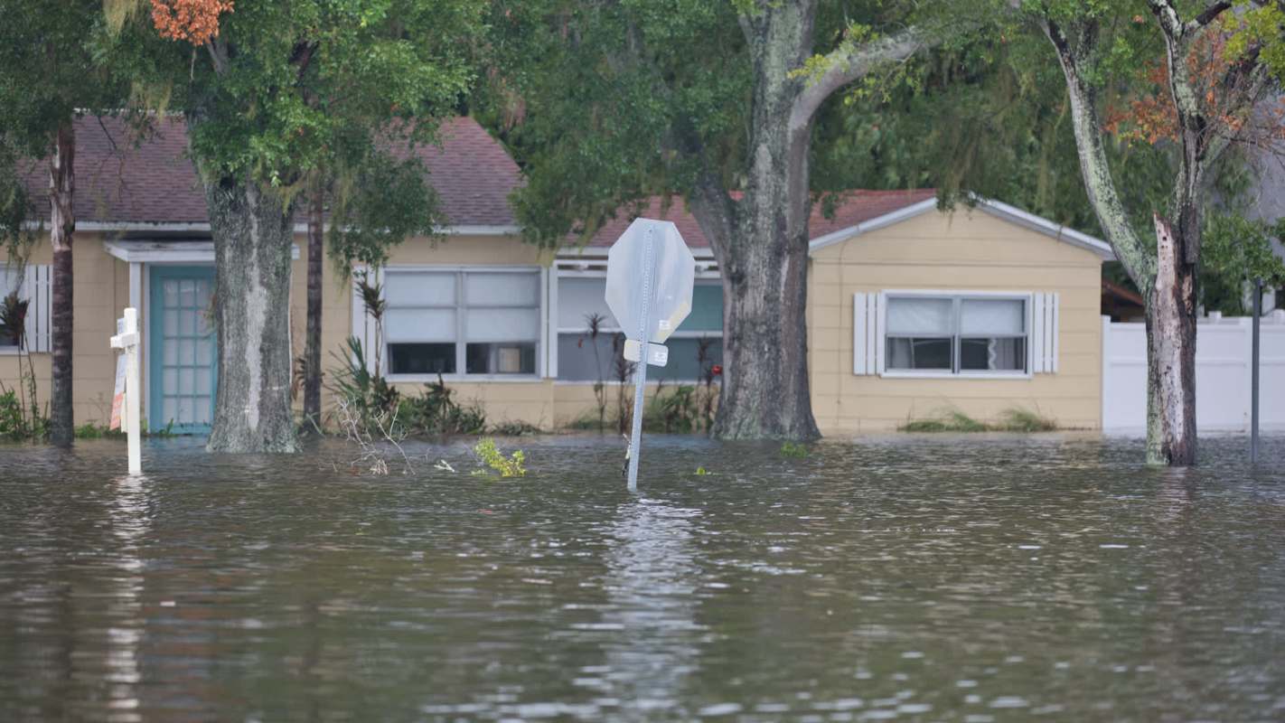A flooded residential area with partially submerged houses and a stop sign.