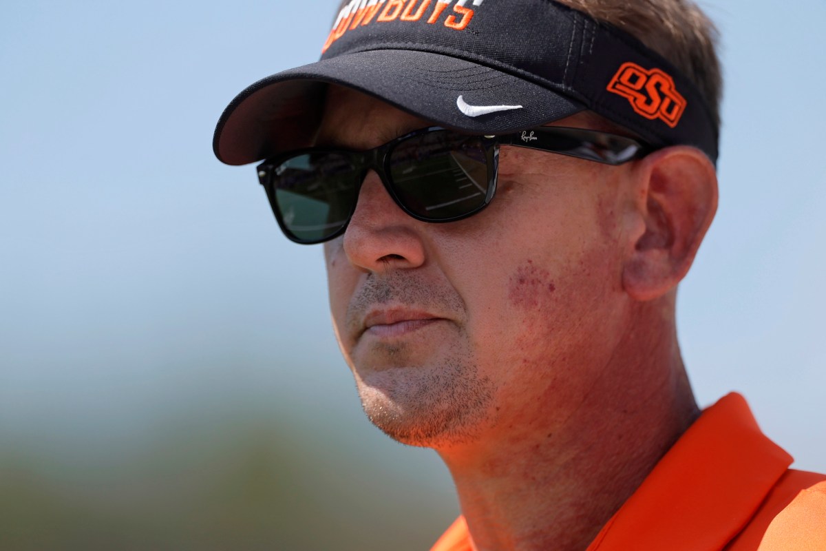 Oklahoma State coach Eric Morris wearing sunglasses and a visor standing outdoors.