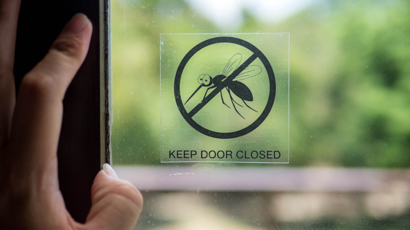 A sign on a window warns to keep the door closed to prevent mosquitoes from entering.