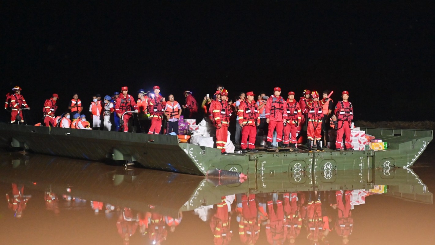 A group of rescue personnel in red uniforms stands on a boat at night, with supplies visible on board.