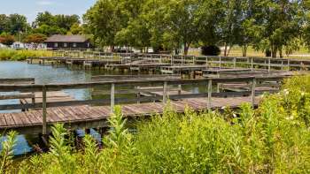 A series of wooden docks extending over a calm body of water, surrounded by greenery and trees.