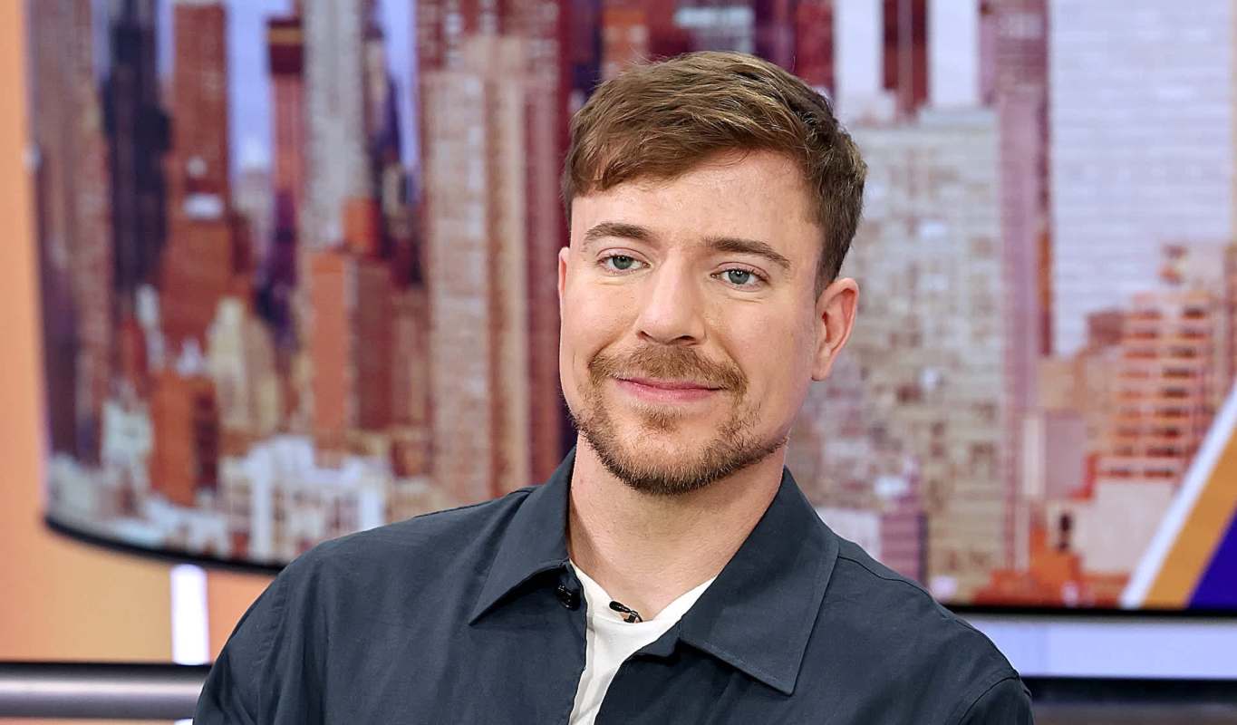 Mr. Beast wearing a dark jacket sits in front of a blurred city skyline.