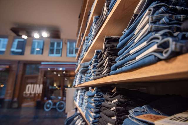 Stacks of folded jeans on wooden shelves inside a MUD clothing store.
