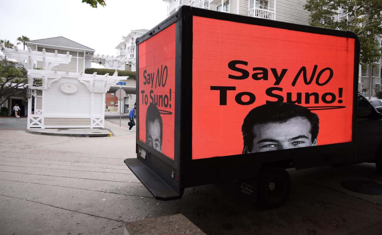 A parked truck displays a large red advertisement reading "Say NO To Suno!" featuring a black and white image of a man.