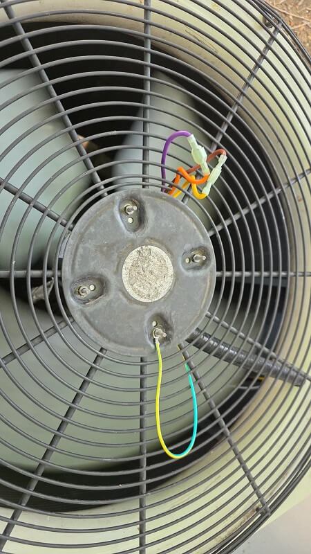 A outdoor fan unit with colorful electrical wires connected to its base.