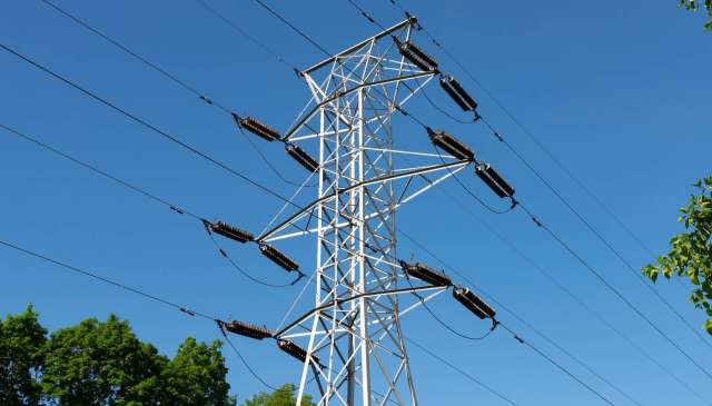 A tall electrical transmission tower with numerous wires against a clear blue sky.