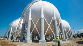 Three large spherical tanks supported by concrete pillars with a worker holding plans nearby.