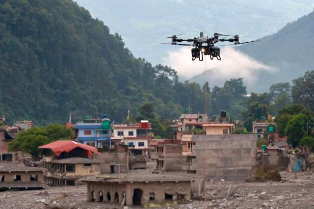 A drone flying over a landscape of damaged buildings and greenery in a mountainous area.