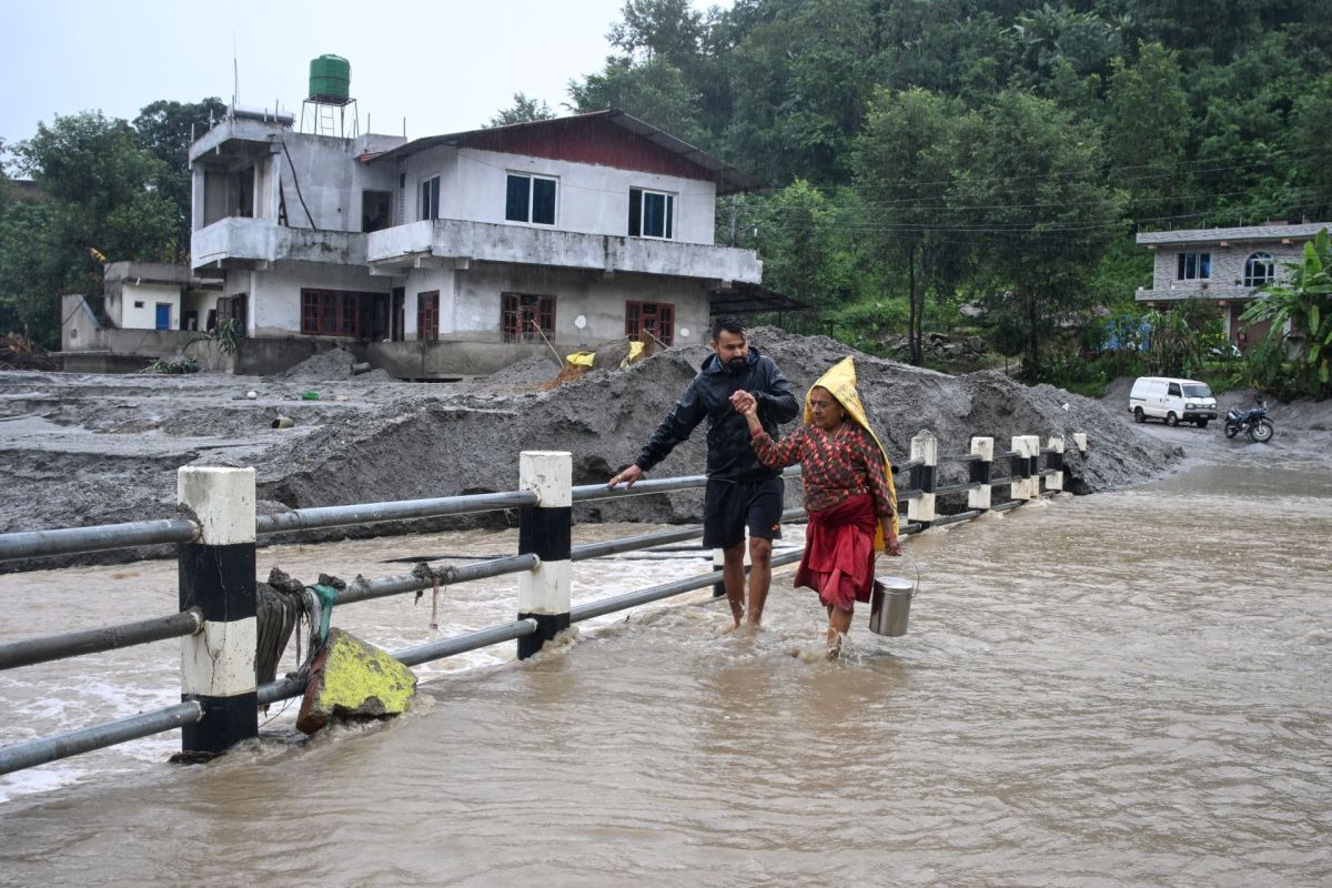 Two people walking across a bridge after a flood in Nepal.