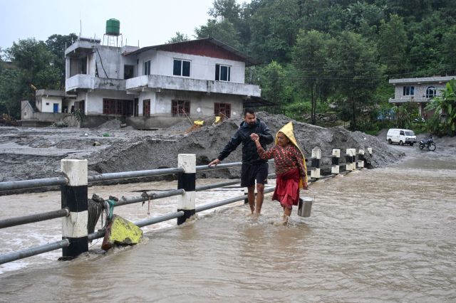 Two people walking across a bridge after a flood in Nepal.