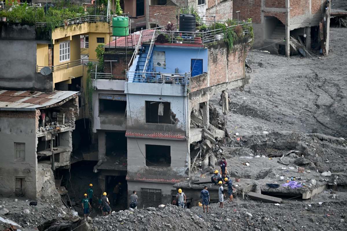 A group of people in hard hats near collapsed buildings amid debris and damaged structures.