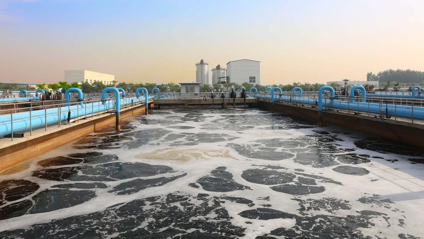 A water treatment facility with large tanks and foamy water in the foreground.