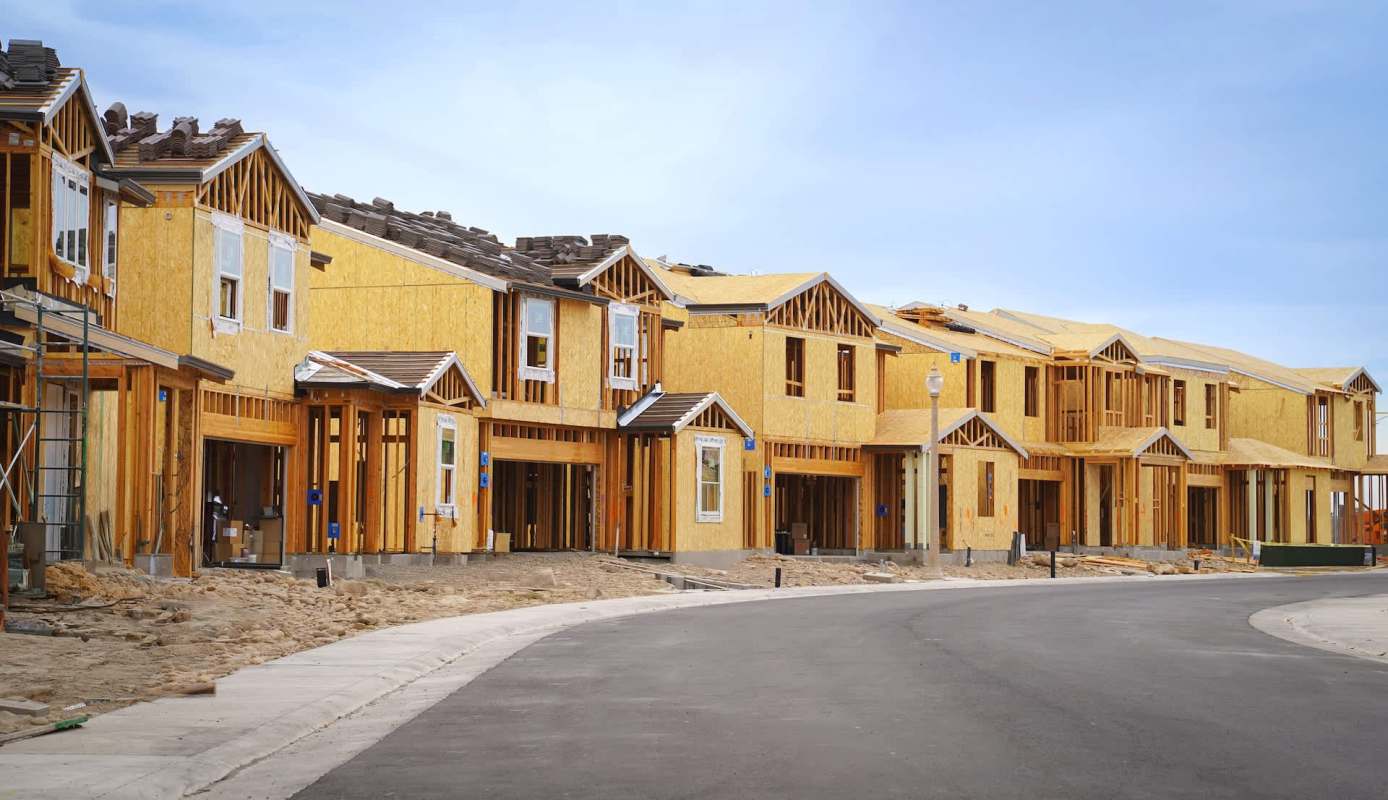 A row of partially constructed houses with wooden frames along a paved road.