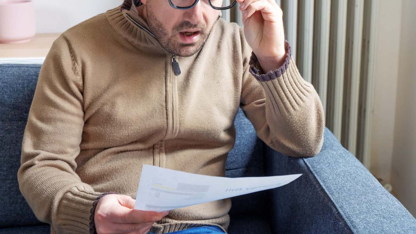 A man sits on a couch, looking surprised while reading a document.