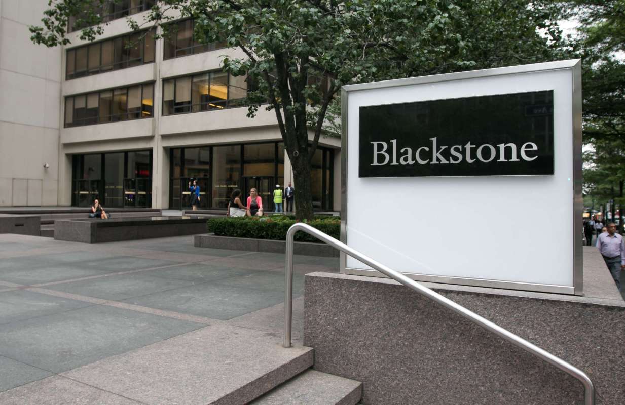 A sign for Blackstone in front of a modern building with people walking by.