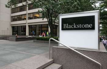 A sign for Blackstone in front of a modern building with people walking by.