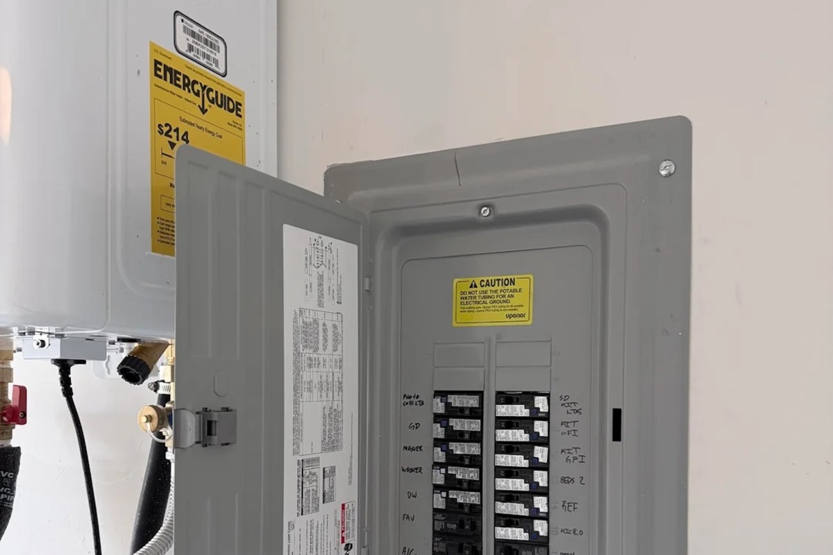 An electrical panel with a caution sign next to a water heating unit, both mounted on a wall.