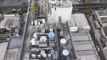 An aerial view of buildings and rooftop equipment, including air conditioning units and satellite dishes, with a road in the background.