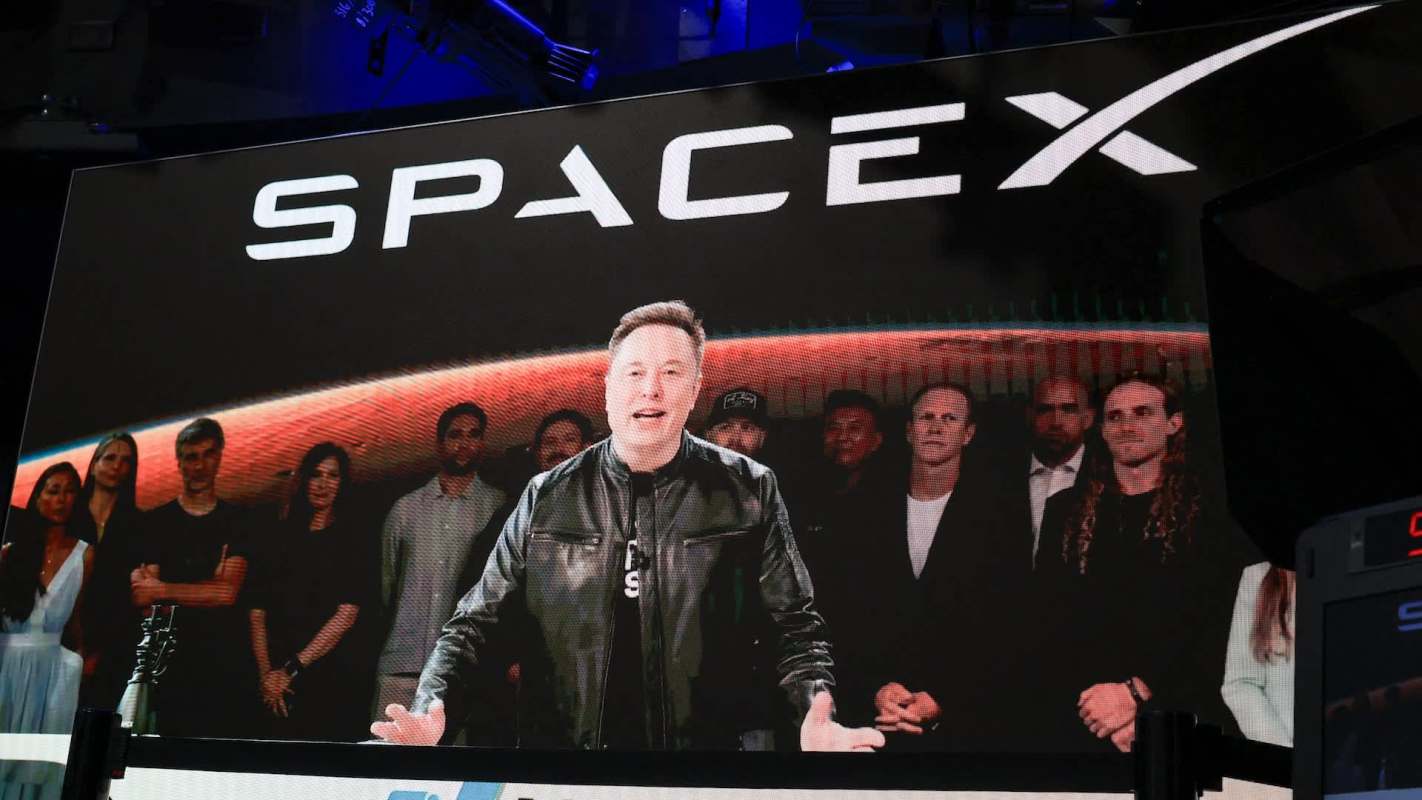 Elon Musk speaking in front of the SpaceX logo.