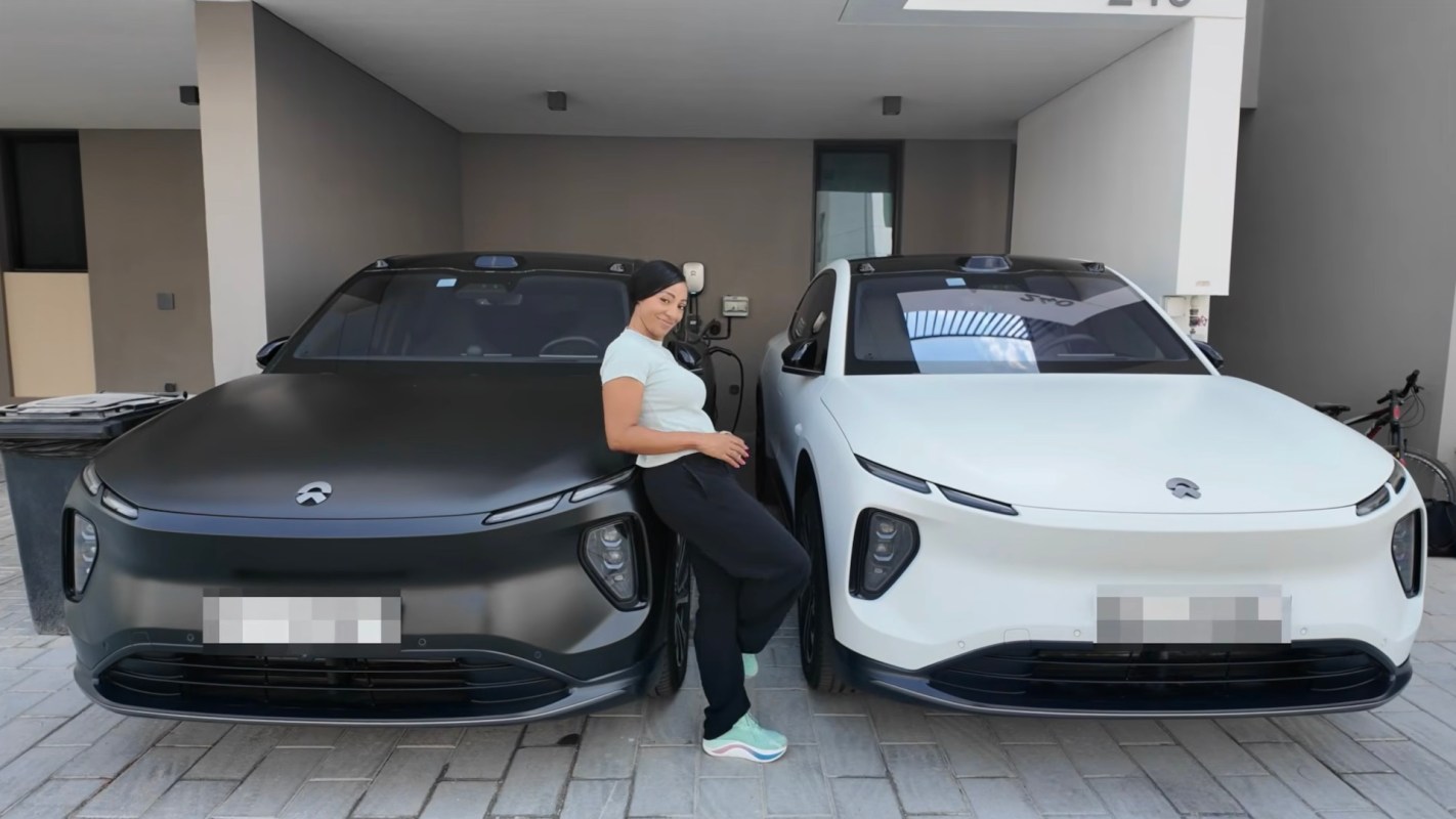 A woman stands between a black and a white electric car in a modern garage.