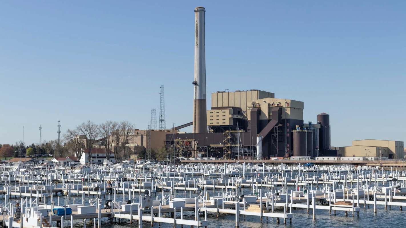 A power plant stands next to a marina filled with numerous white boat docks.