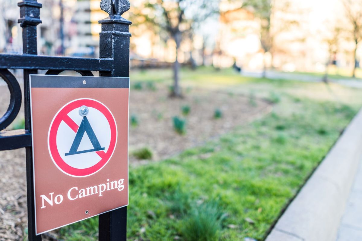 A sign on a fence displaying a "No Camping" message in a park setting.