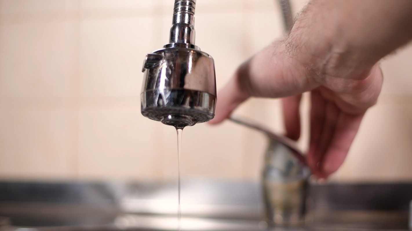 A hand adjusts a faucet that is dripping water in a kitchen setting.
