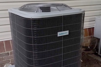 An outdoor air conditioning unit beside a house, featuring a metal grille and a label.