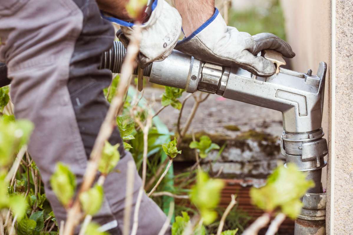 A person in gloves adjusts a metal pipe among greenery.