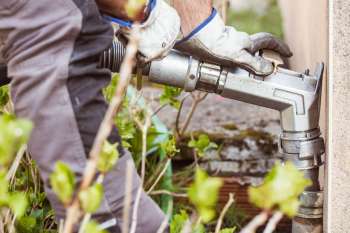 A person in gloves adjusts a metal pipe among greenery.