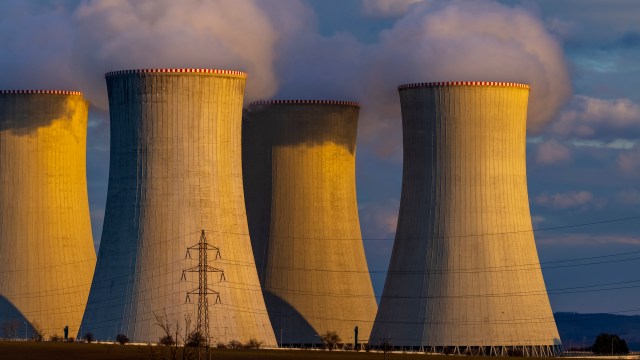 Four cooling towers release steam against a cloudy sky with power lines in the foreground.