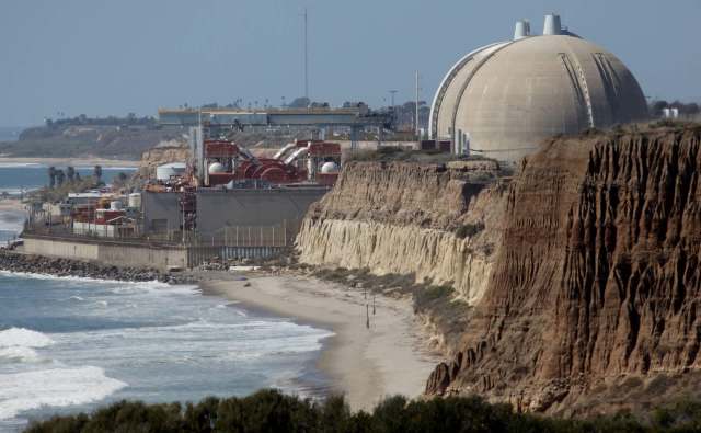 The San Onofre nuclear power plant located near a beach with rocky cliffs and waves.