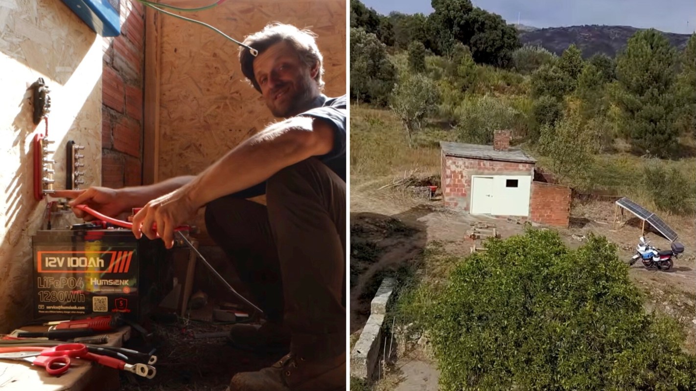 A man works on electrical connections next to a large battery in a rustic interior, with tools on the floor.