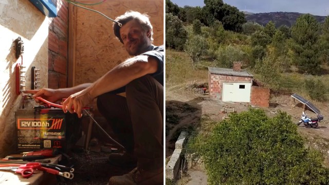 A man works on electrical connections next to a large battery in a rustic interior, with tools on the floor.