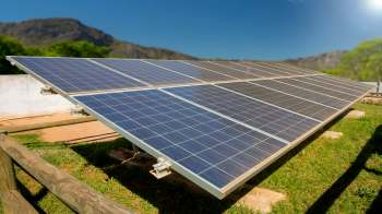 A solar panel array installed on a grassy area with mountains in the background.