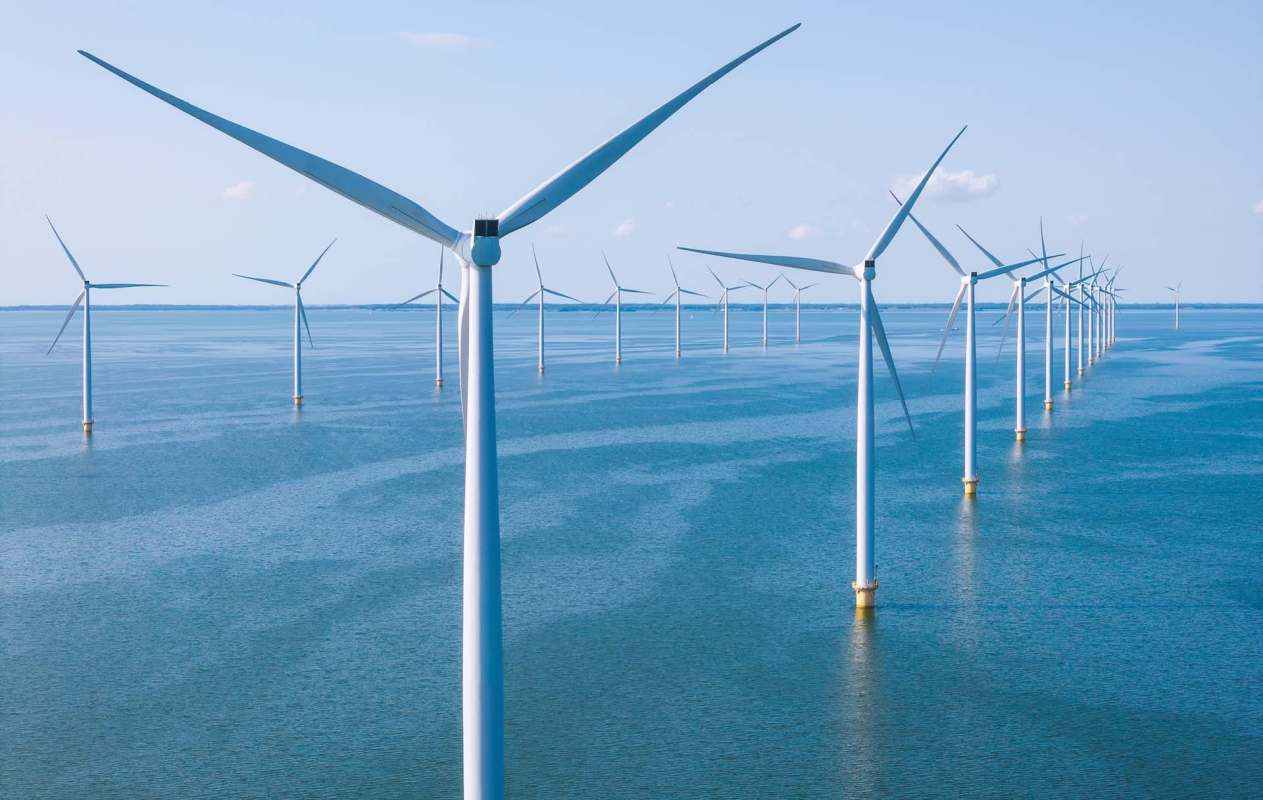A row of wind turbines stands in a vast body of water under a clear blue sky.