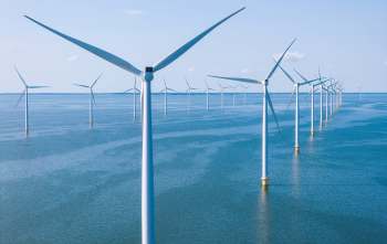 A row of wind turbines stands in a vast body of water under a clear blue sky.