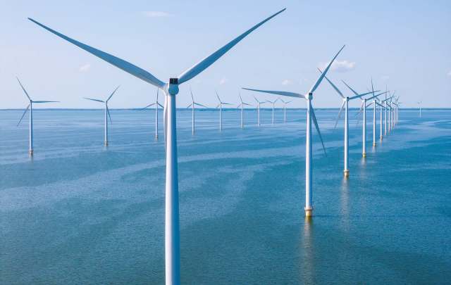 A row of wind turbines stands in a vast body of water under a clear blue sky.