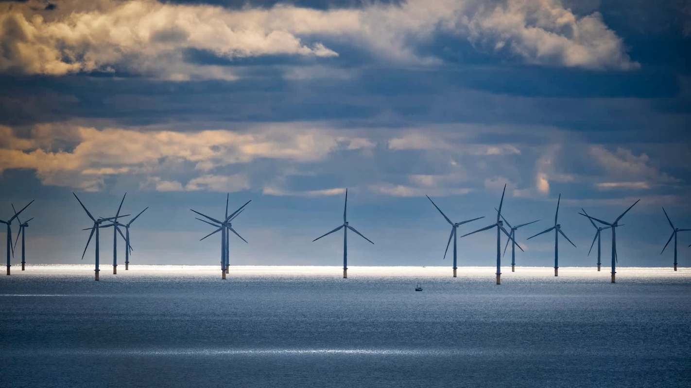 Wind turbines line the horizon in a body of water under cloudy skies.