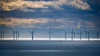 Wind turbines line the horizon in a body of water under cloudy skies.