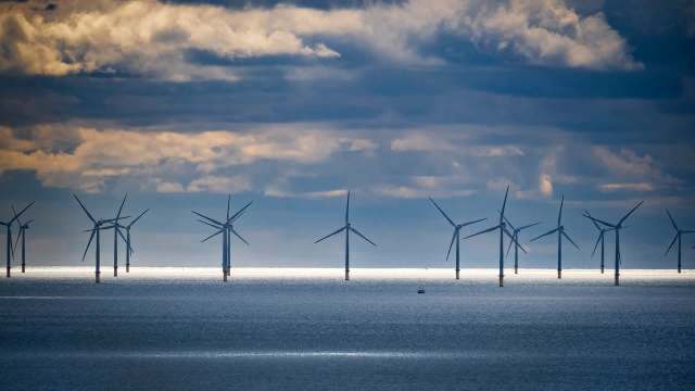 Wind turbines line the horizon in a body of water under cloudy skies.