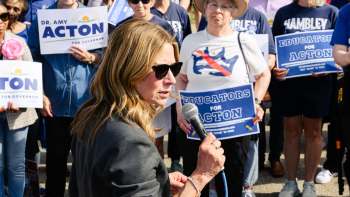 Ohio Democratic gubernatorial candidate Amy Acton speaks into a microphone with supporters holding political signs.