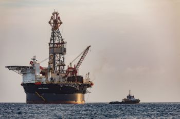 An oil drilling platform with a tugboat in the ocean.