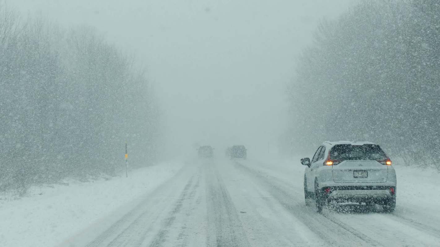 A snowy road with two vehicles driving through heavy snowfall.