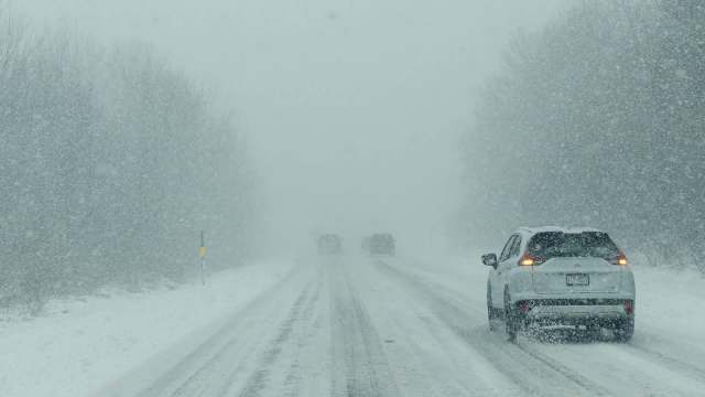 A snowy road with two vehicles driving through heavy snowfall.